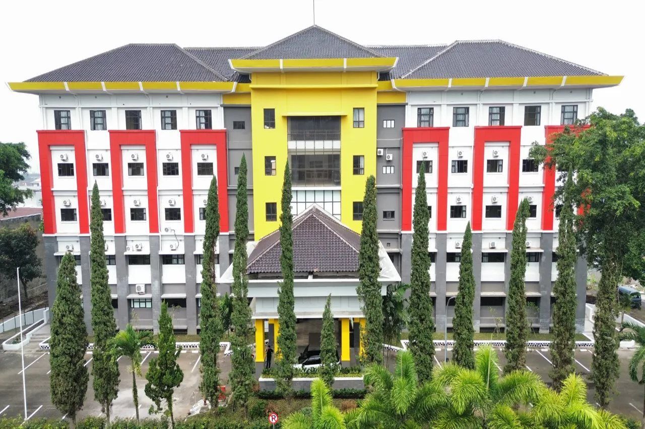 A multi-story building with a central yellow section and red accents, surrounded by greenery.