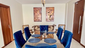 Een eetruimte met een houten tafel, zes blauwe fauteuils en twee aan de muur hangende schilderijen.