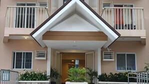 Un edificio de varios pisos con una entrada central, escalones de piedra y plantas en macetas.