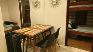 Una habitación pequeña con una mesa y sillas de madera, una cama con estructura de madera y dos relojes de pared.