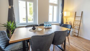 Un comedor con una mesa de madera, sillas tapizadas de gris, una planta en maceta y un ventanal con cortinas.