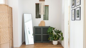 Un pasillo con un espejo grande, una planta en maceta, un adorno de macramé en la pared y una colección de cuadros enmarcados.