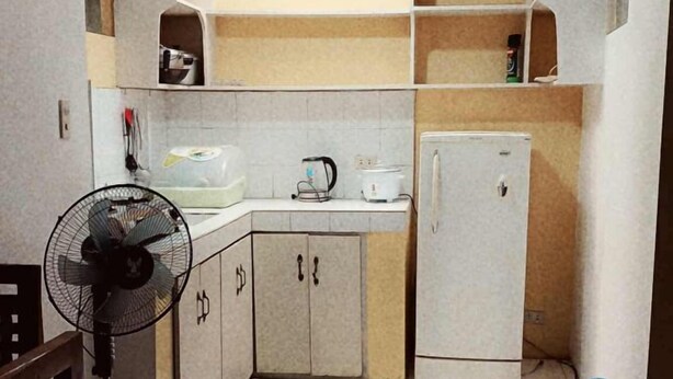 Una cocina con refrigerador, microondas y ventilador. Hay un dispensador de agua y una botella de agua grande en el suelo.