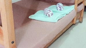 Una cama litera con colchón y almohadas rosadas, una manta verde y dos almohadas a rayas.