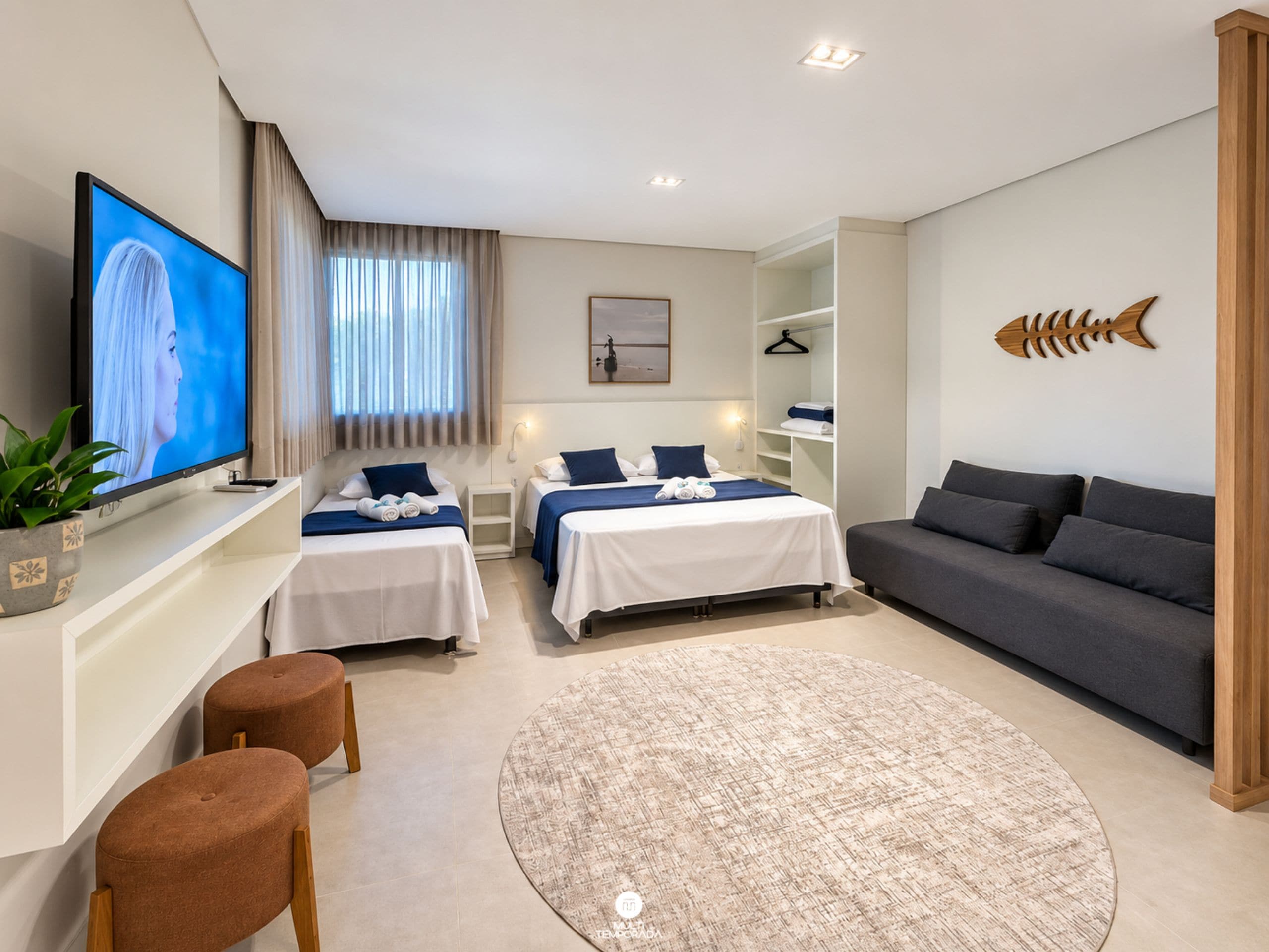 Habitación de hotel moderna con dos camas, un sofá, un televisor y una pieza decorativa de arte mural con peces.