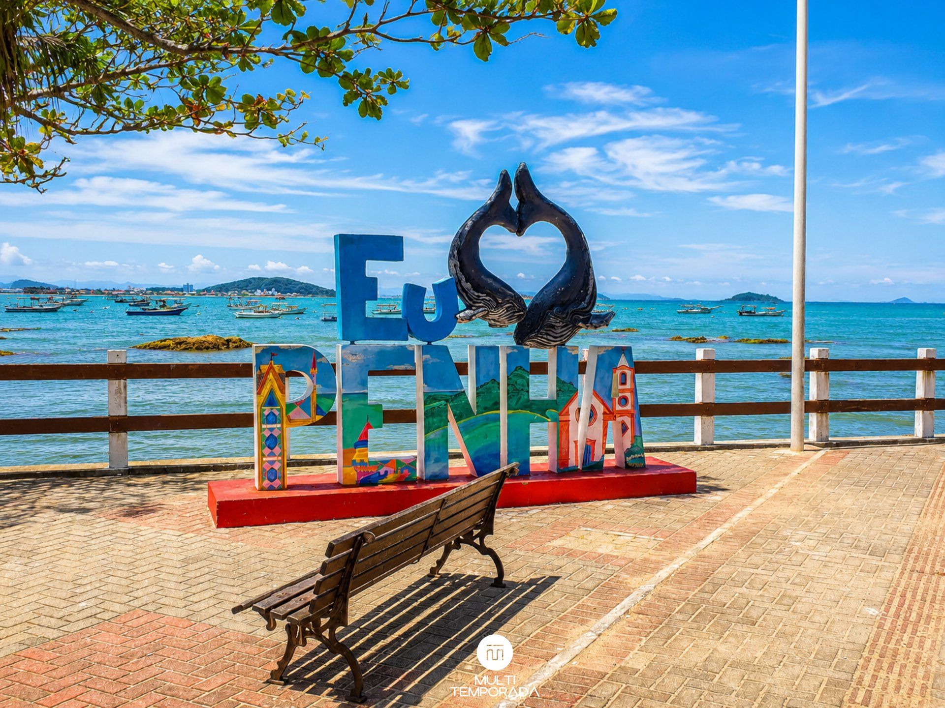 Un banco, un cartel que dice 'Eu PENINA' y una escultura de ballena, con vista al frente marítimo.