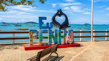 Un banco, un cartel que dice 'Eu PENINA' y una escultura de ballena, con vista al frente marítimo.