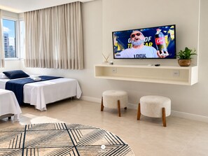 Quarto de hotel moderno com uma cama, televisão na parede, um pequeno espaço para sentar e vista para a cidade pela janela.