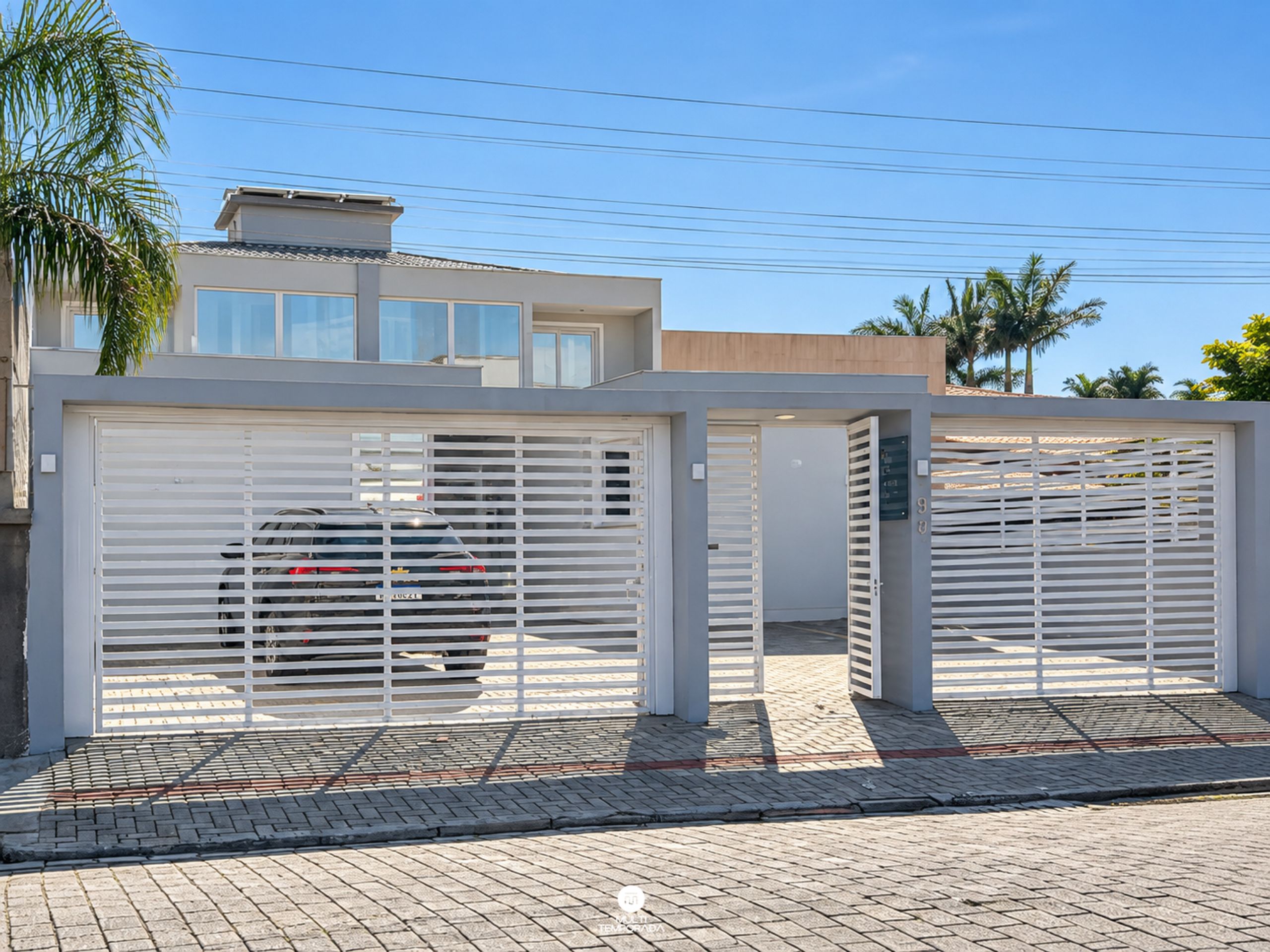Uma casa moderna de dois andares com garagem, um carro estacionado dentro e um acesso pavimentado.