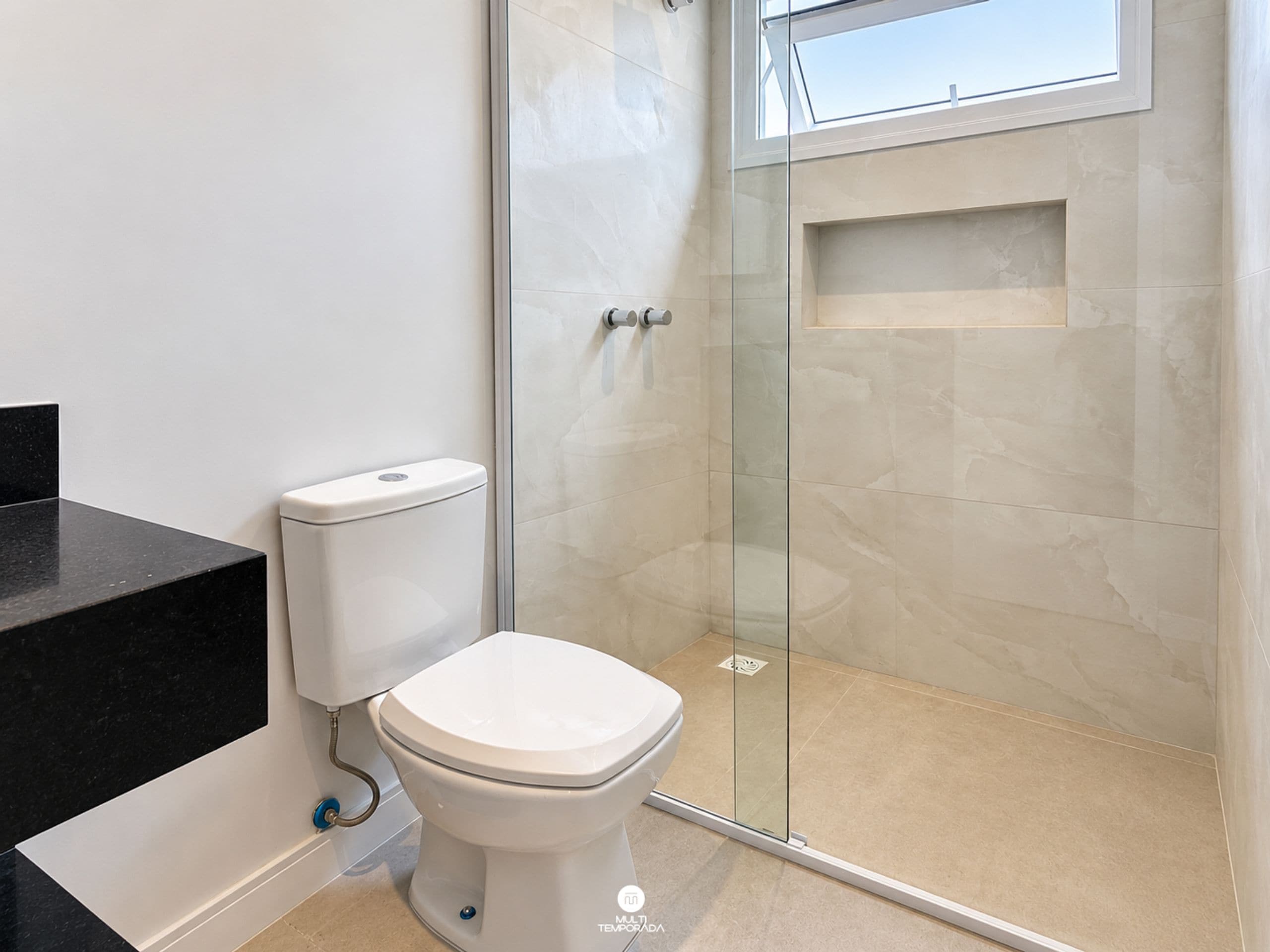 Un baño moderno con inodoro, cabina de ducha de vidrio y encimera negra.