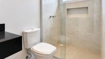 Un baño moderno con inodoro, cabina de ducha de vidrio y encimera negra.