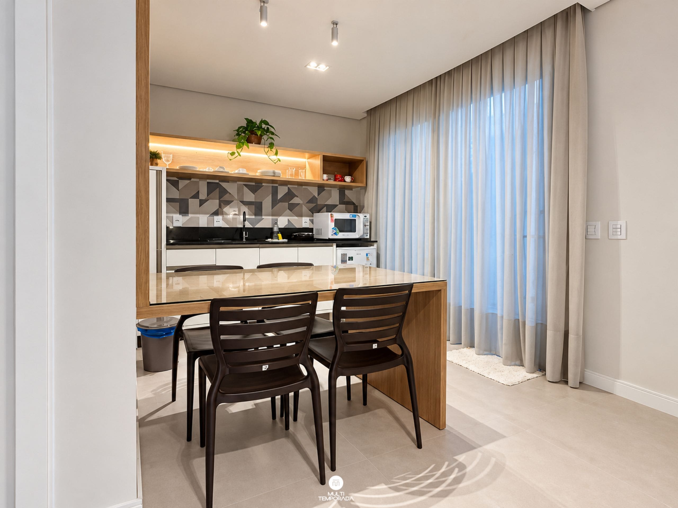 Una cocina moderna con una isla central, dos sillas y un microondas.