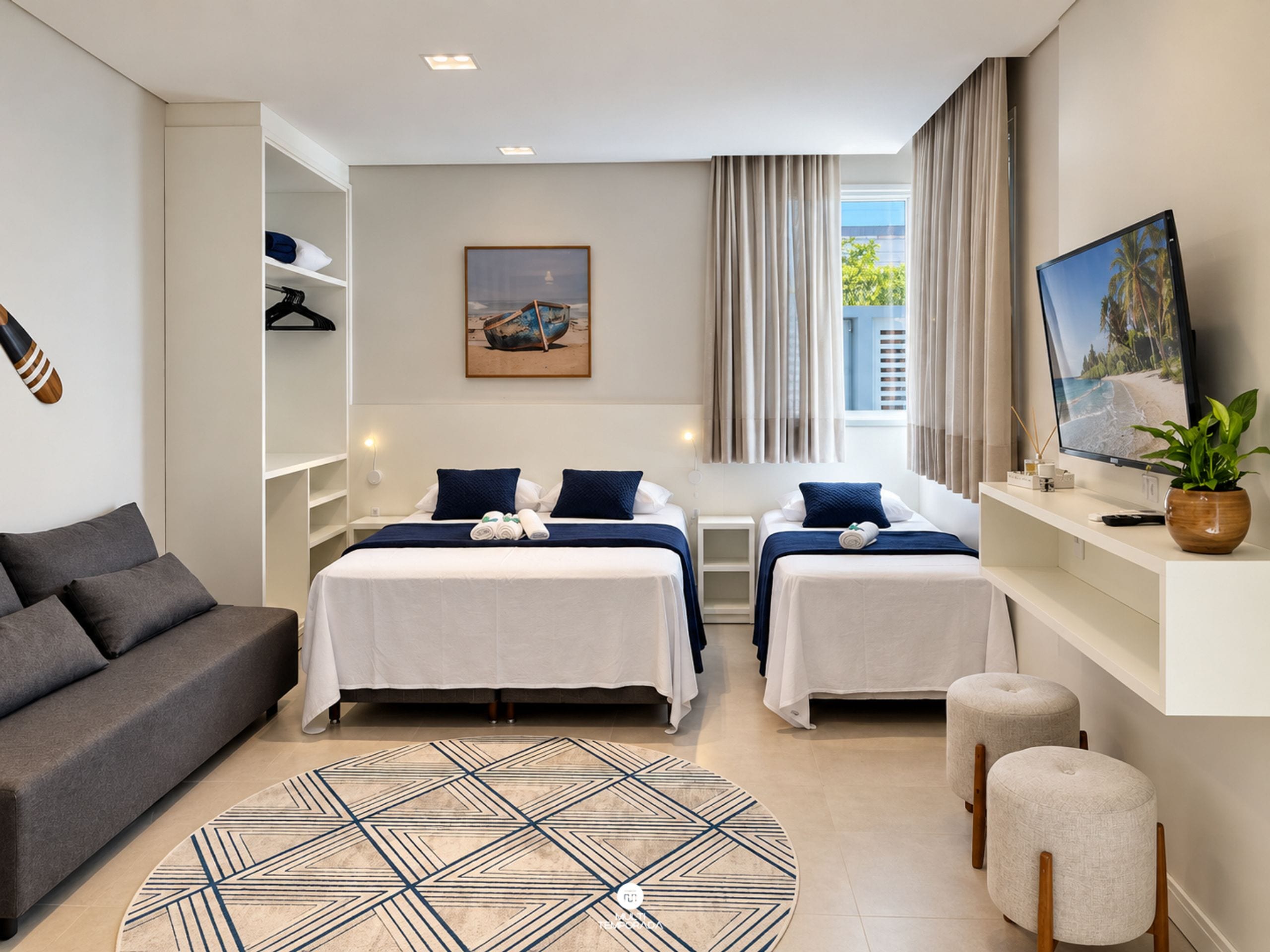 Quarto de hotel com cama, sofá, televisão e janela com cortinas.