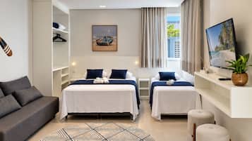 Quarto de hotel com cama, sofá, televisão e janela com cortinas.