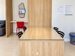 A modern meeting room with a wooden table, black chairs, a red chair, a white desk, and a mirror on the wall. - D'Santa Lofts - Penha - SC (Penha)