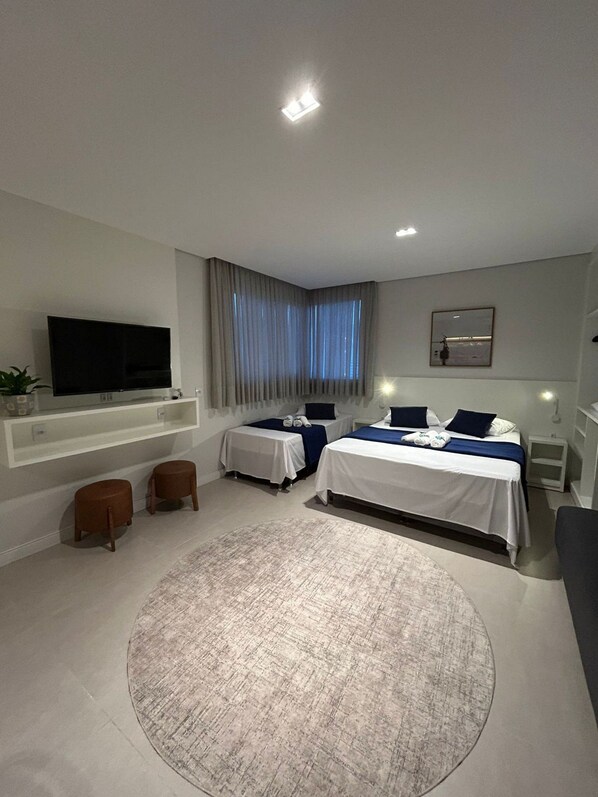 A modern hotel room with two beds, a flat-screen TV, a large window with curtains, a round rug, and a small seating area. - D'Santa Lofts - Penha - SC (Penha)