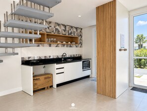 A modern kitchen with a black countertop, white cabinets, and a built-in oven. There is a wooden panel on the wall and a door leading outside. - D'Santa Lofts - Penha - SC (Penha)