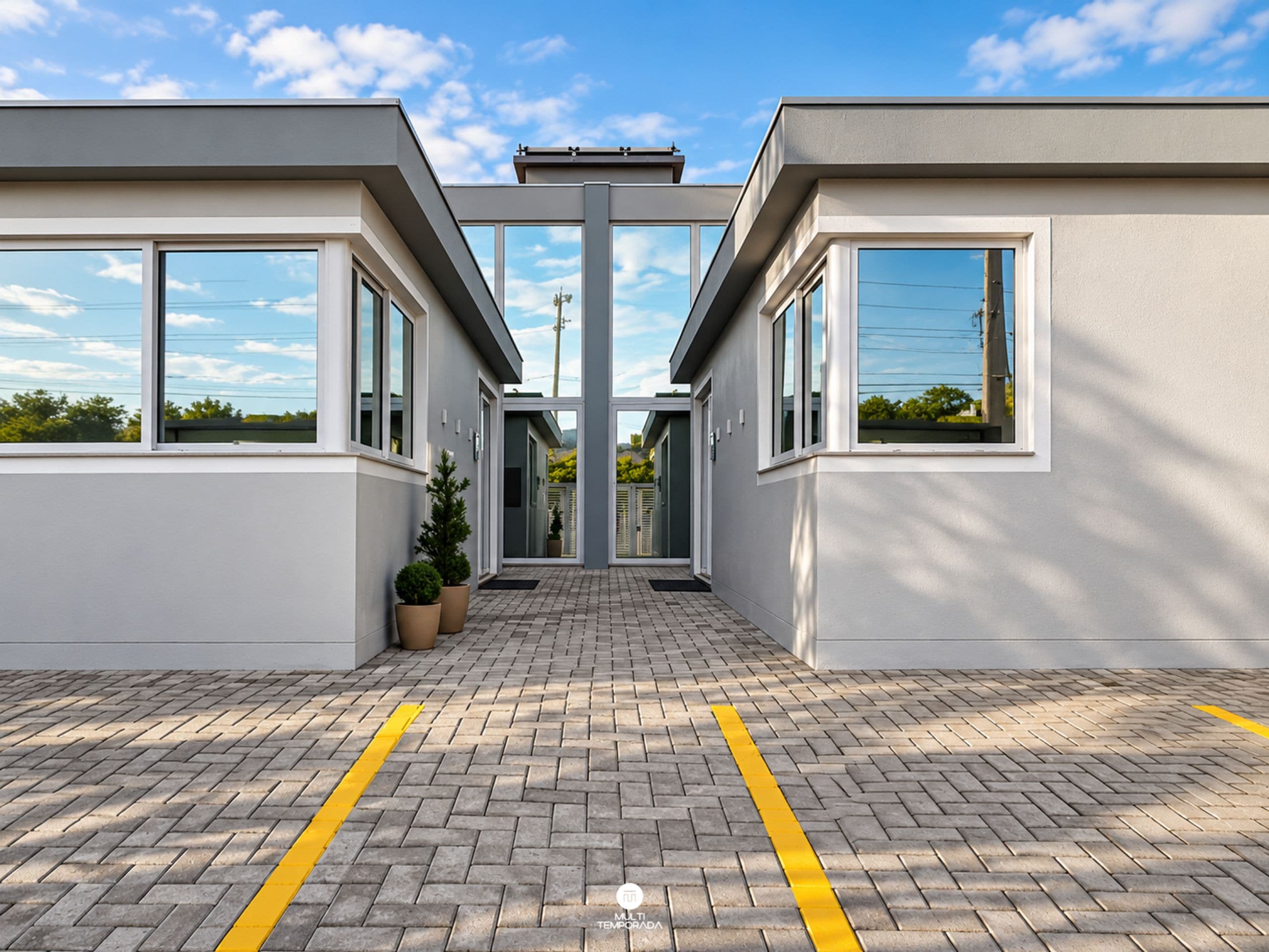 Um edifício moderno com fachada simétrica, grandes janelas e área de entrada pavimentada.