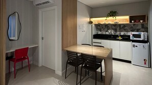 A modern kitchen with white cabinets, a microwave, and a refrigerator. There is a dining table with chairs and a red chair in the corner. - D'Santa Lofts - Penha - SC (Penha)