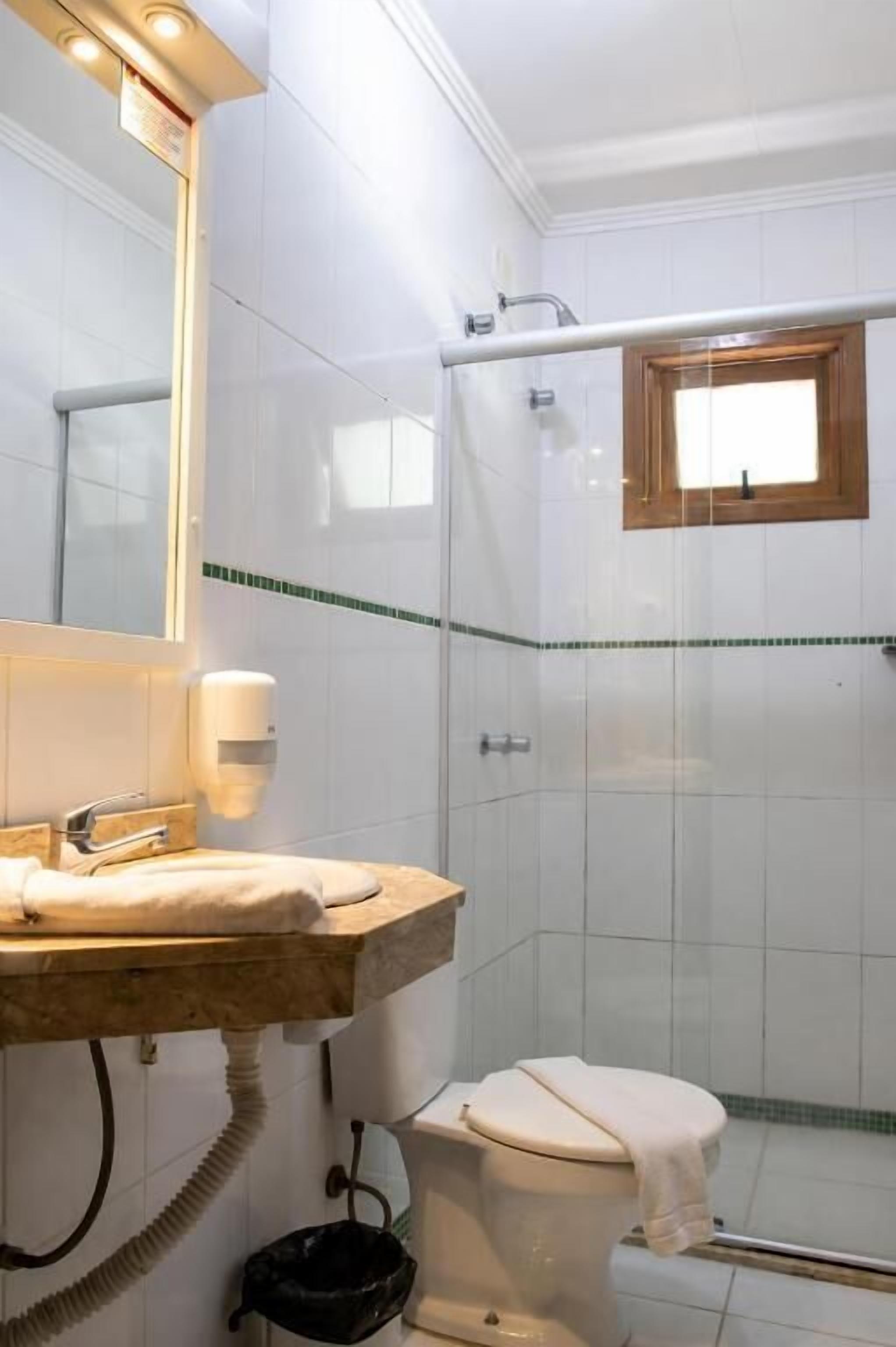 Un baño con ducha de vidrio, inodoro, lavamanos con toalla y espejo con iluminación.