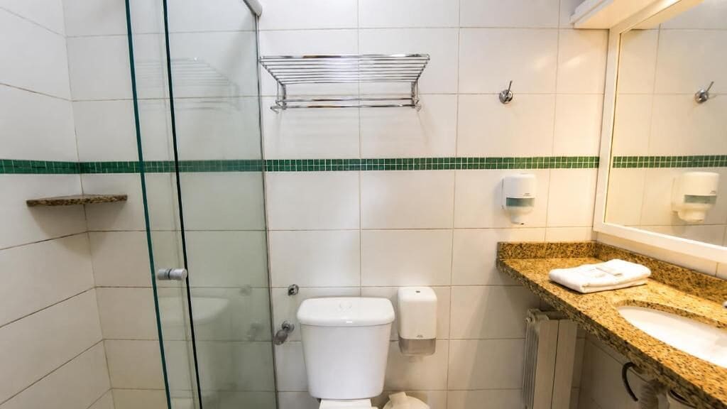 A bathroom with a glass shower enclosure, a toilet, a sink with a granite countertop, and a mirror.