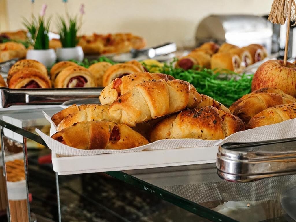 Un bufé con diversas opciones de panadería, incluyendo cruasanes y panes, dispuestas en bandejas.