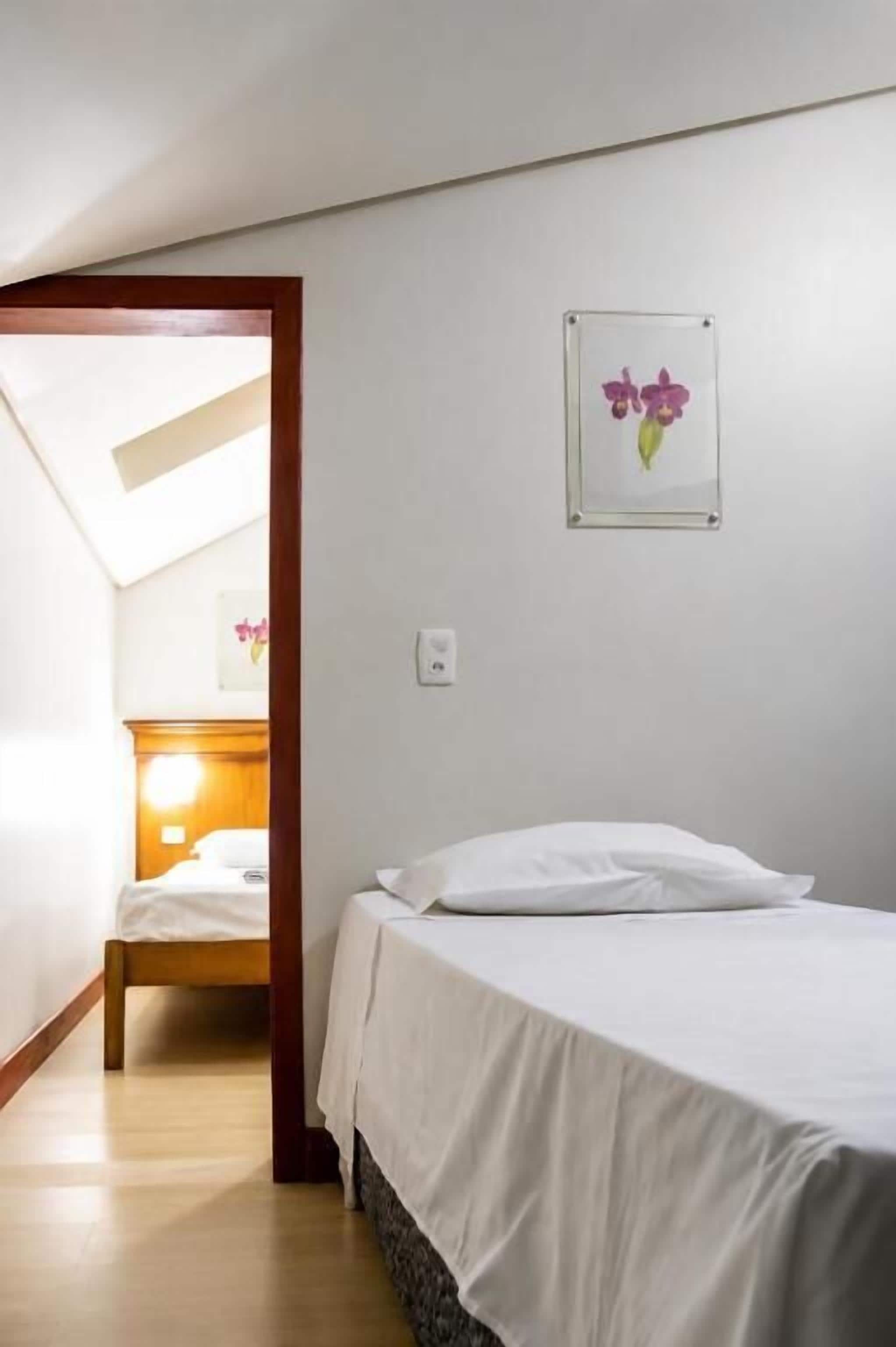 A bedroom with a bed, a nightstand, a wall-mounted picture, and a door leading to another room.