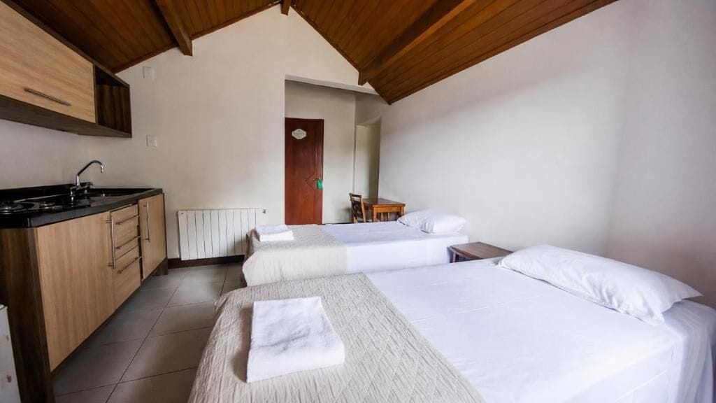 Habitació amb dos llits, petita cuina i sostre de fusta.