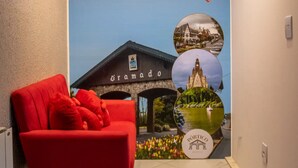 Un couloir avec une chaise rouge, une affiche murale représentant un bâtiment portant l’inscription « Tramado », et un logo pour « Portico Hotel ».