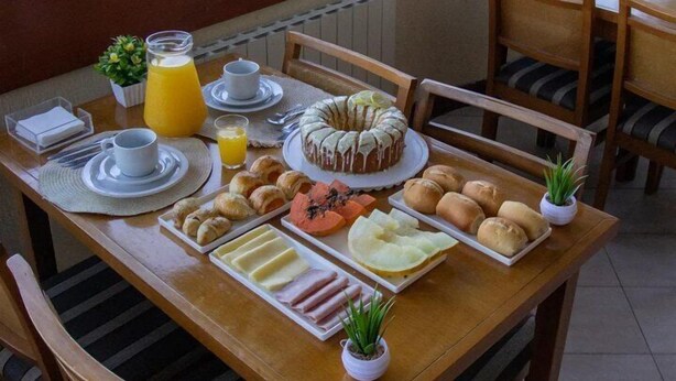 Une table de petit-déjeuner avec des assiettes remplies de nourriture, une carafe de jus et une vue sur l’extérieur.