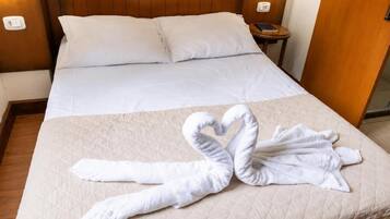 Quarto de hotel com uma cama, almofadas, mesa de cabeceira com telefone e luminária na parede.