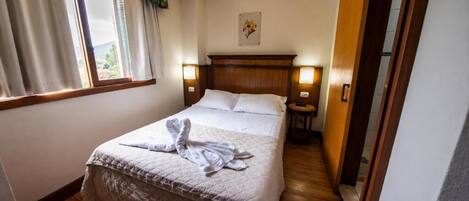 A hotel room with a bed, bedside lamps, a window with curtains, and a wooden floor.