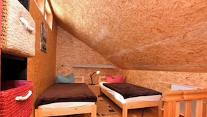 Un dormitorio abrigado en el ático con dos camas de madera, un escritorio pequeño y una cesta roja.