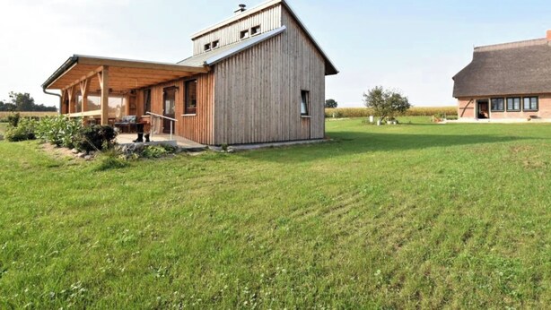 Una casa moderna de madera con un porche cubierto y un amplio campo abierto al fondo.