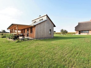 A modern wooden house with a covered porch and a large open field in the background. - Pure nature in lakeside holiday home (Rühn)