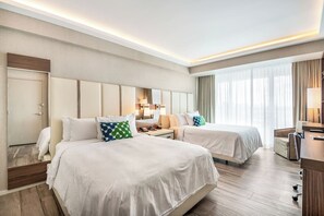 Habitación de hotel con dos camas, un escritorio, una silla y un ventanal grande.