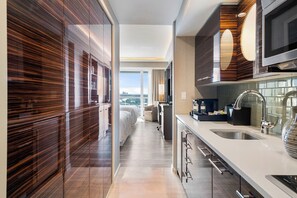 Habitación de hotel moderna con cocina, un amplio ventanal y vistas a la ciudad, además de una zona de dormitorio independiente.