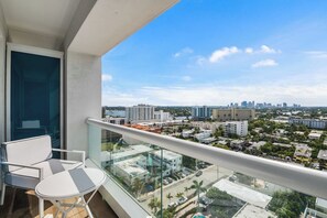 A balcony with a glass railing overlooking a cityscape with buildings and a clear sky. - Conrad Private Residence | Ocean & Intracoastal Views | 2 Queens (Fort Lauderdale)
