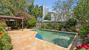 A rectangular swimming pool with a tiled edge, surrounded by a patio with beige tiles.