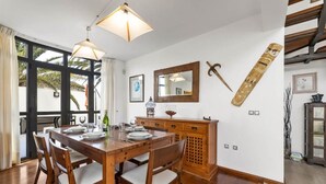 A dining area with a wooden table and chairs, pendant lights, a wooden cabinet, and a large window with curtains. - Villa Paula - Three Bedroom Villa, Sleeps 6 (Costa Teguise)