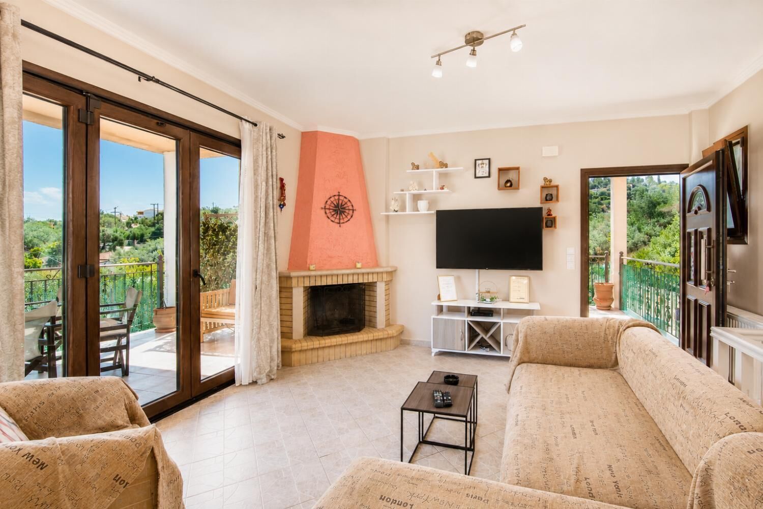 Ein Wohnzimmer mit Kamin, einer Couch, einem Fernseher und einem Balkon mit Gartenmöbeln.
