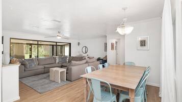 A modern living room with a wooden dining table, light blue chairs, a grey sofa, and a ceiling fan.