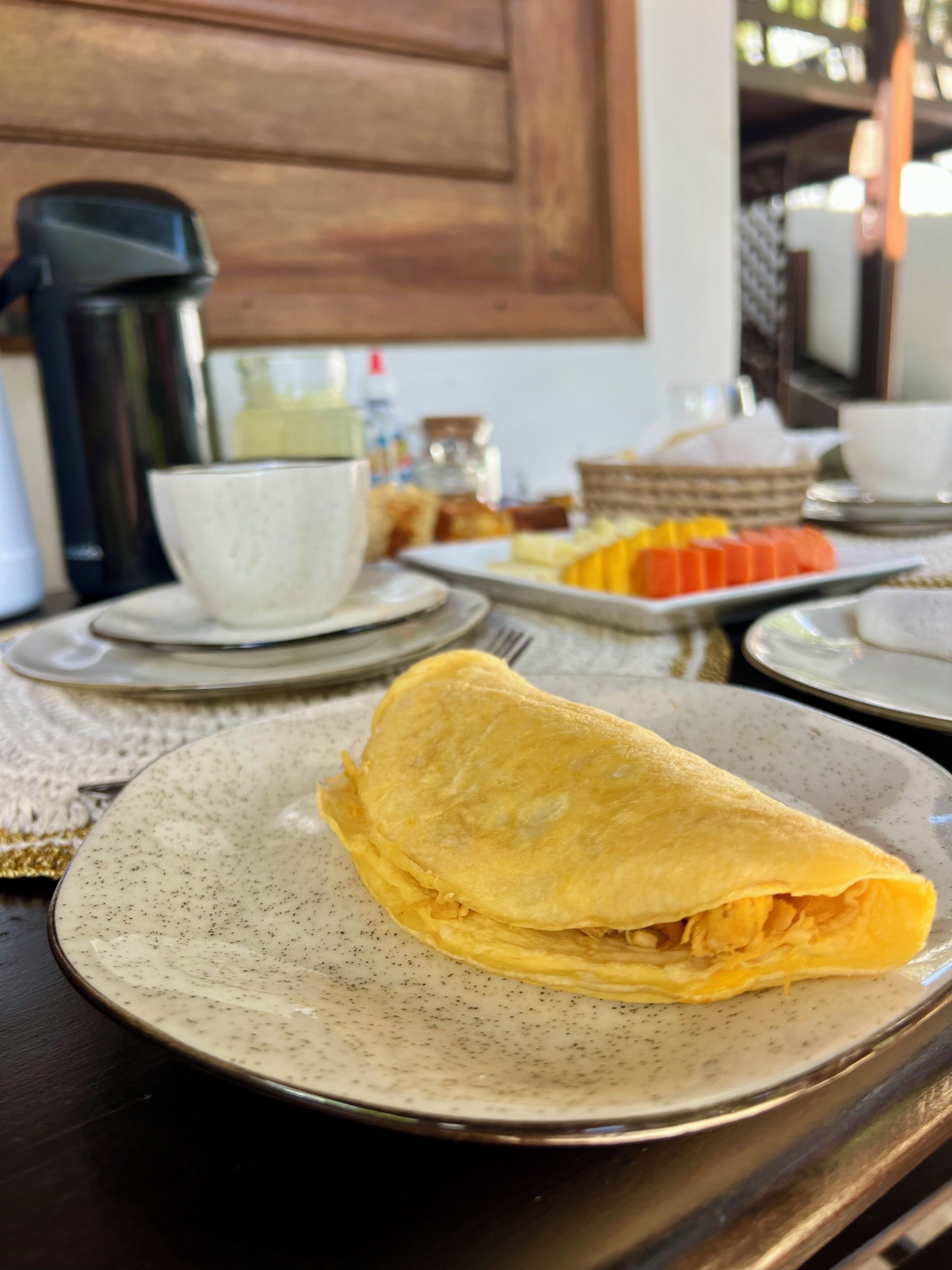 A breakfast setting with a folded omelette on a plate, a coffee pot, and a basket of pastries.