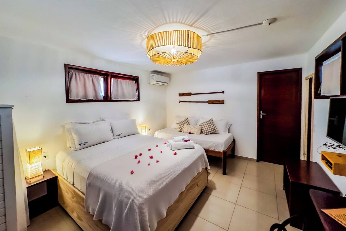 A hotel room with a bed, bedside tables, a desk, a chair, a television, and a ceiling light fixture.