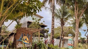 A resort with a large building, palm trees, and a sign with a sun and waves design. - aky jeri pousada  (Jijoca de Jericoacoara)