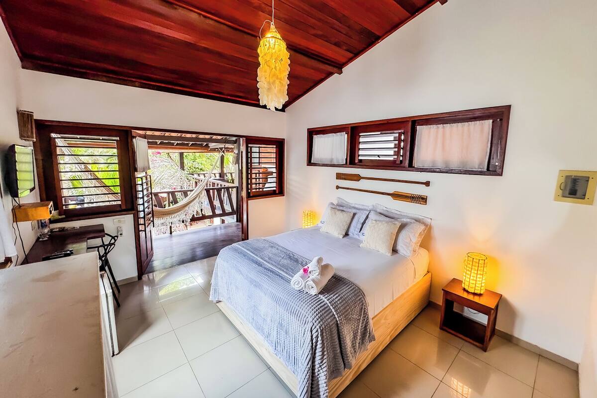 A bedroom with a bed, bedside lamps, a desk, a chair, and a hammock.