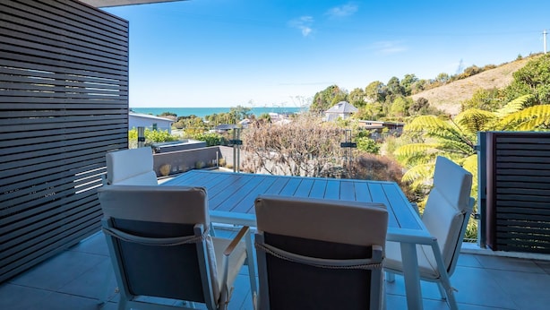 Une terrasse avec deux chaises et une table, offrant une vue panoramique sur un paysage vallonné et la mer.
