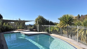 Une piscine dotée d’une terrasse en bois et d’une clôture en métal, entourée d’arbres et surplombée par un ciel dégagé.