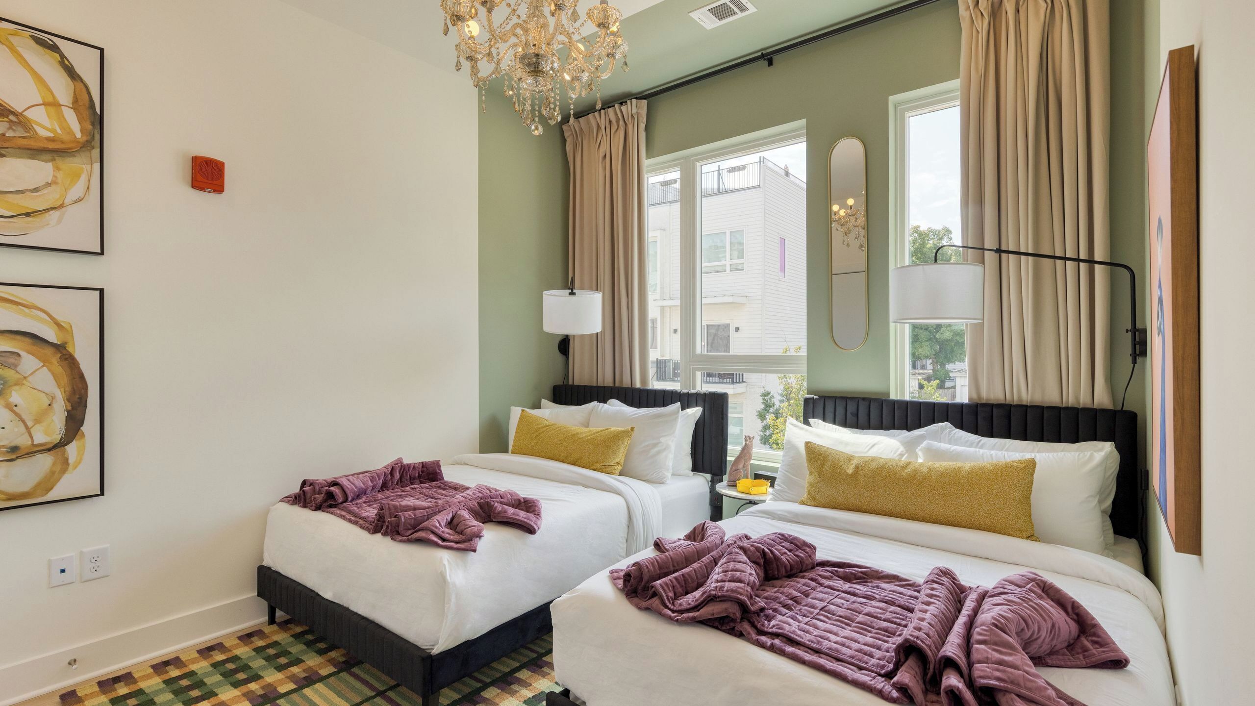 Hotelkamer met twee bedden, een kroonluchter, een raam met gordijnen en kunstwerken aan de wanden.