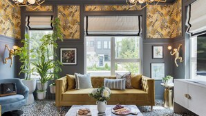 A cozy living room with a sofa, a coffee table with snacks, and a large window with a view of the outside.